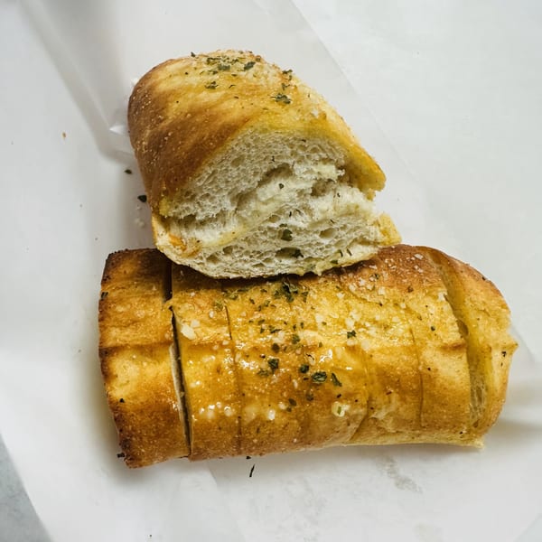 Golden-brown garlic bread, sliced and seasoned with herbs, on white parchment paper.
