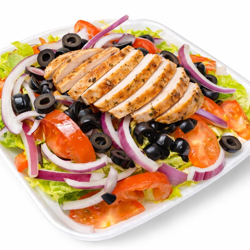 Grilled chicken salad with lettuce, tomatoes, red onions, and black olives in a white container.