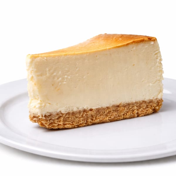 A slice of classic New York cheesecake with a golden crust on a white plate.